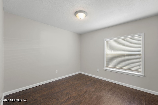 spare room with a textured ceiling, dark wood-type flooring, and baseboards