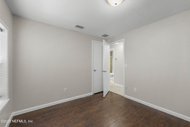 unfurnished bedroom with visible vents, a textured ceiling, baseboards, and wood finished floors