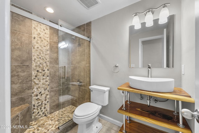 bathroom with toilet, a sink, visible vents, baseboards, and a shower stall