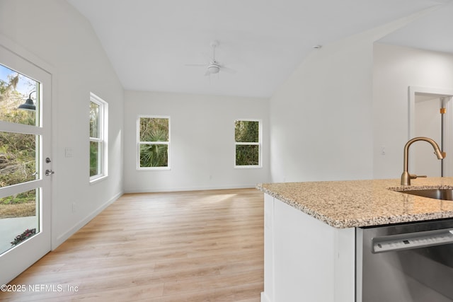 kitchen featuring lofted ceiling, light stone countertops, light wood-type flooring, stainless steel dishwasher, and a sink