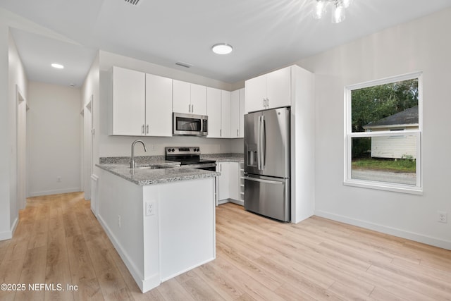 kitchen with light stone counters, light wood finished floors, stainless steel appliances, a sink, and a peninsula