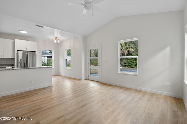 unfurnished living room with lofted ceiling, ceiling fan, light wood-style flooring, visible vents, and baseboards