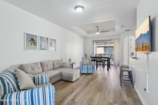 living room with arched walkways, a raised ceiling, ceiling fan, wood finished floors, and baseboards