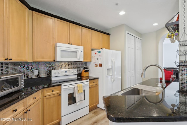 kitchen featuring tasteful backsplash, dark stone counters, a sink, light wood-type flooring, and white appliances