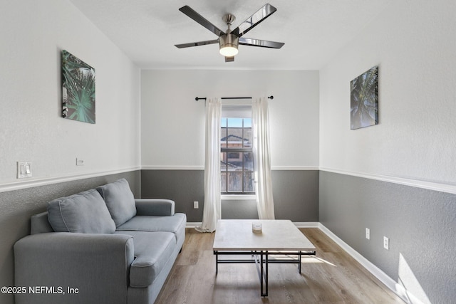 living area featuring a textured wall, ceiling fan, baseboards, and wood finished floors