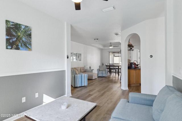 living room with a ceiling fan, arched walkways, light wood-type flooring, and visible vents