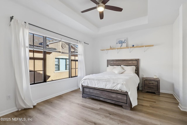 bedroom featuring a tray ceiling, wood finished floors, and baseboards