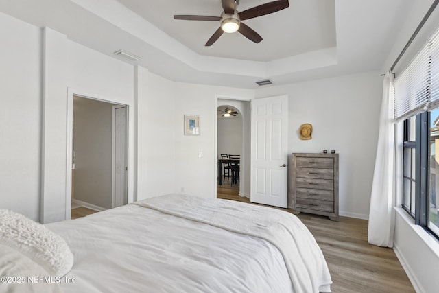 bedroom featuring light wood finished floors, multiple windows, a raised ceiling, and visible vents