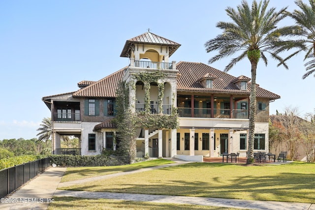 view of front of property with a balcony, fence, a tiled roof, stucco siding, and a front yard