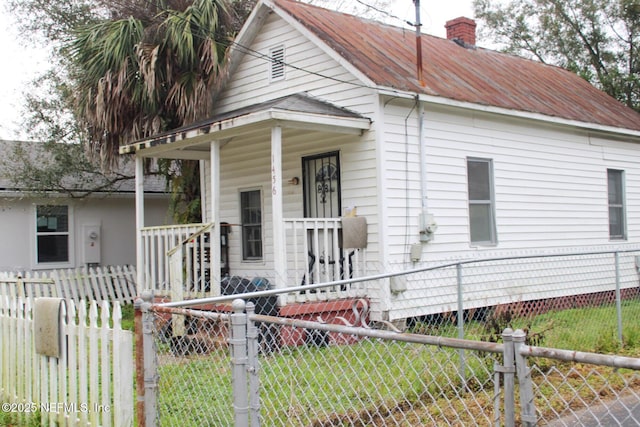 bungalow-style house with covered porch, metal roof, a chimney, and a fenced front yard