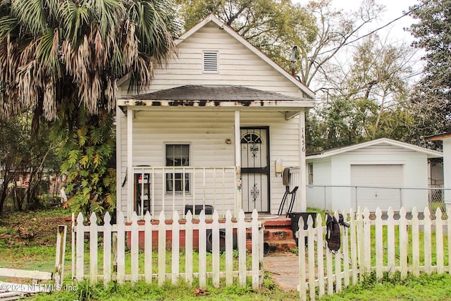 shotgun-style home featuring a fenced front yard, a detached garage, a shingled roof, a porch, and an outdoor structure