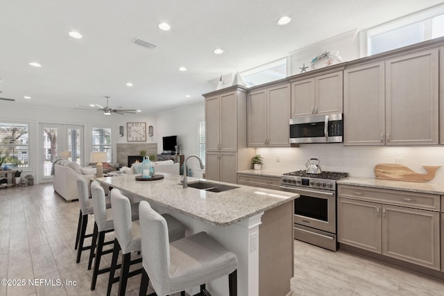 kitchen with a sink, visible vents, a lit fireplace, appliances with stainless steel finishes, and tasteful backsplash