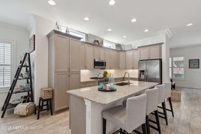 kitchen with a sink, appliances with stainless steel finishes, light stone countertops, a kitchen bar, and crown molding