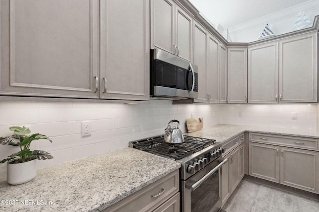 kitchen with light stone counters, appliances with stainless steel finishes, gray cabinets, tasteful backsplash, and crown molding