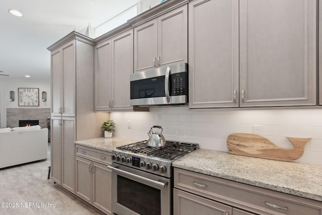 kitchen featuring stainless steel appliances, gray cabinets, a lit fireplace, and tasteful backsplash