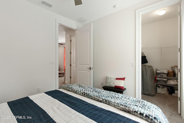 carpeted bedroom featuring a spacious closet, a closet, visible vents, and a ceiling fan