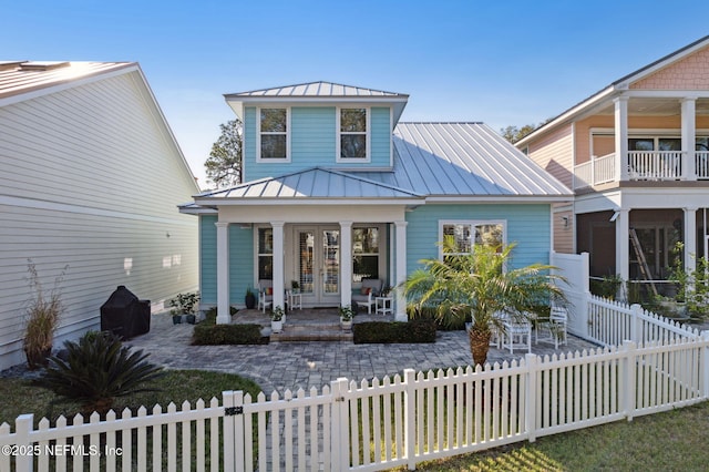 view of front of home featuring metal roof, a fenced front yard, covered porch, french doors, and a standing seam roof