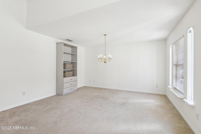 empty room featuring light carpet, a textured ceiling, visible vents, and an inviting chandelier