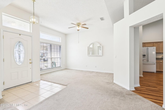 entryway featuring light carpet, visible vents, a ceiling fan, a high ceiling, and a textured ceiling