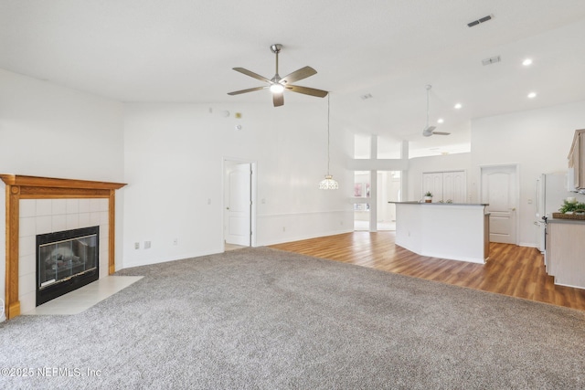 unfurnished living room with carpet, visible vents, a ceiling fan, high vaulted ceiling, and a tile fireplace