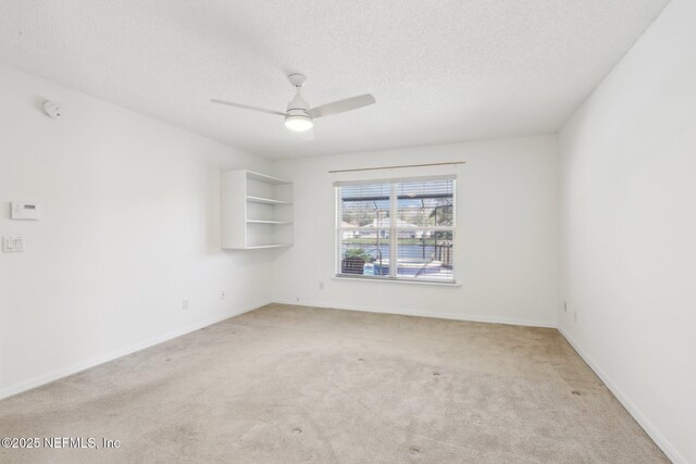 empty room featuring ceiling fan, baseboards, a textured ceiling, and light colored carpet