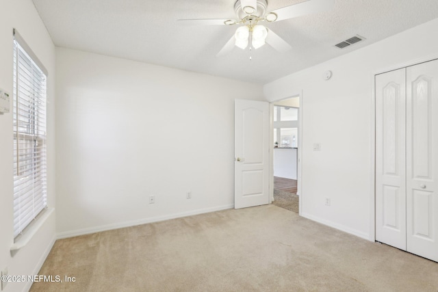 unfurnished bedroom featuring a textured ceiling, carpet floors, visible vents, baseboards, and a closet