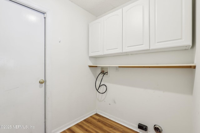 laundry area with hookup for a washing machine, cabinet space, baseboards, and wood finished floors