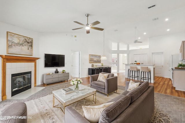 living room with visible vents, a tile fireplace, ceiling fan, light wood-type flooring, and recessed lighting