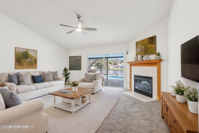 carpeted living room featuring vaulted ceiling, a tiled fireplace, and a ceiling fan