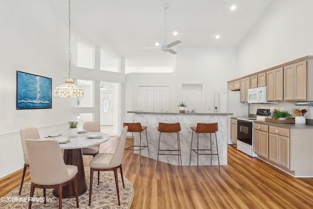 kitchen with white appliances, a kitchen island with sink, a high ceiling, light wood-style floors, and a kitchen bar