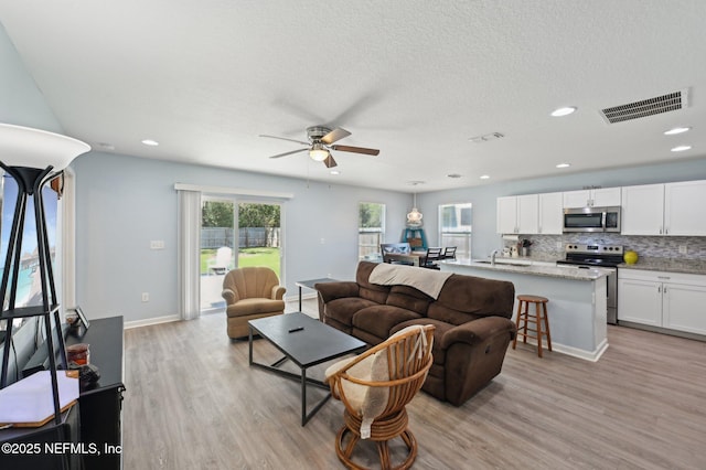 living area with baseboards, light wood-style flooring, visible vents, and a textured ceiling