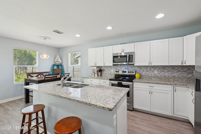 kitchen with tasteful backsplash, stainless steel appliances, light wood-style floors, white cabinetry, and a sink