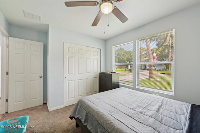 bedroom with a closet, visible vents, a ceiling fan, light carpet, and baseboards