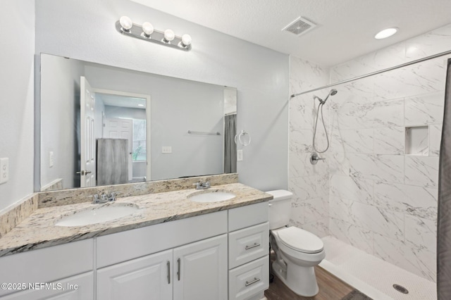 bathroom featuring toilet, a stall shower, a sink, and visible vents