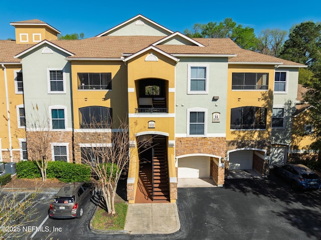 multi unit property featuring a garage, central AC, driveway, and stucco siding