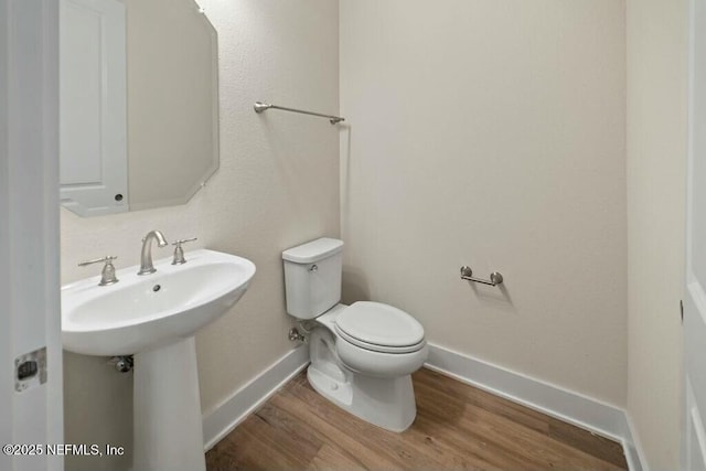 half bathroom featuring a sink, wood finished floors, toilet, and baseboards