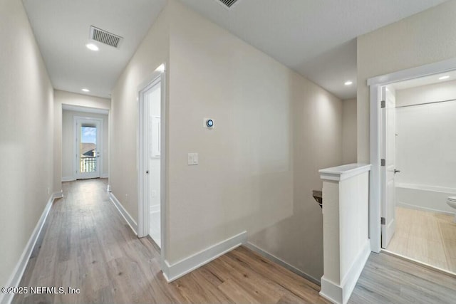 hall featuring visible vents, light wood-style flooring, and an upstairs landing