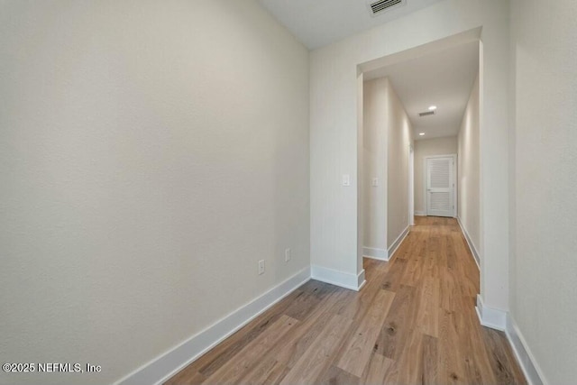 hall featuring baseboards, visible vents, and wood finished floors