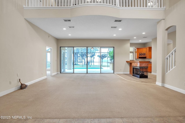 unfurnished living room featuring light colored carpet, a fireplace, visible vents, and a towering ceiling