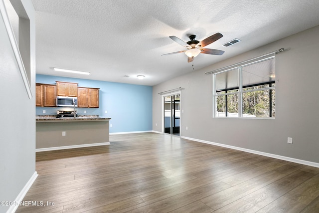 unfurnished living room with ceiling fan, a textured ceiling, visible vents, baseboards, and dark wood finished floors