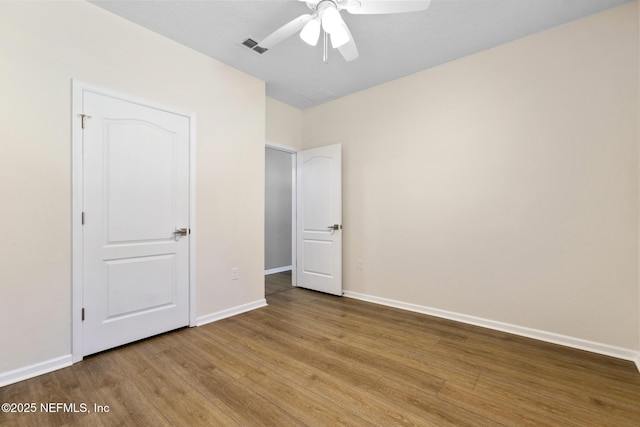 unfurnished bedroom with a ceiling fan, visible vents, baseboards, and wood finished floors