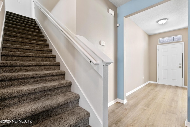 stairway with a textured ceiling, baseboards, and wood finished floors