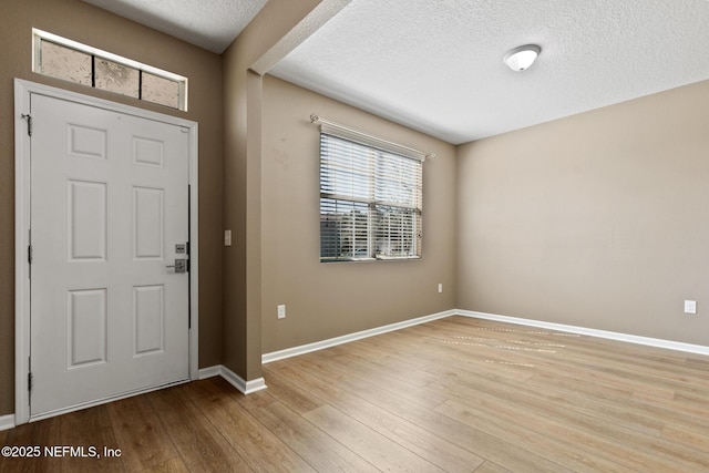 foyer entrance featuring a textured ceiling, baseboards, and wood finished floors