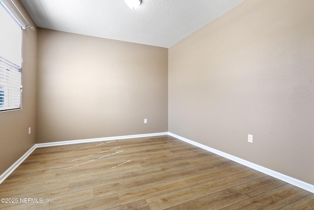 spare room featuring light wood-style flooring, baseboards, and a textured ceiling