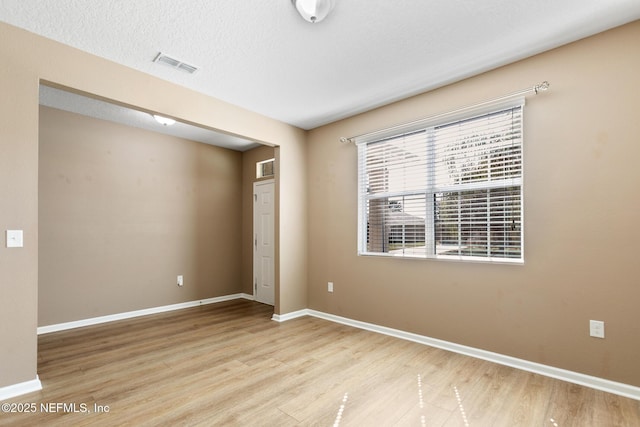 empty room with baseboards, a textured ceiling, visible vents, and wood finished floors