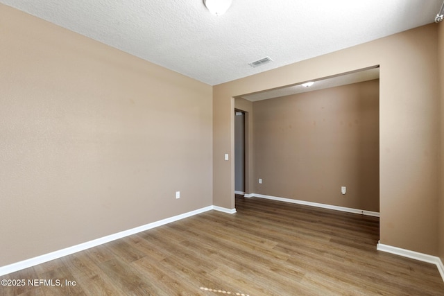 spare room with baseboards, visible vents, a textured ceiling, and light wood finished floors