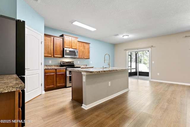 kitchen featuring appliances with stainless steel finishes, brown cabinets, a sink, and light wood finished floors