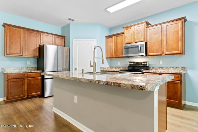 kitchen featuring a center island with sink, light wood finished floors, visible vents, appliances with stainless steel finishes, and a sink