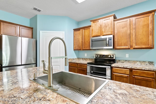 kitchen with visible vents, appliances with stainless steel finishes, brown cabinets, a textured ceiling, and a sink