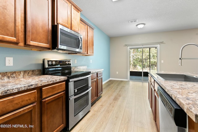 kitchen featuring visible vents, appliances with stainless steel finishes, a textured ceiling, light wood-style floors, and a sink